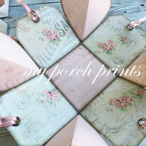 May include: A pink and green paper box with a heart shape design. The box is decorated with floral patterns and French text. The box is open and the inside is visible. The box is made of paper and has a delicate, vintage aesthetic.