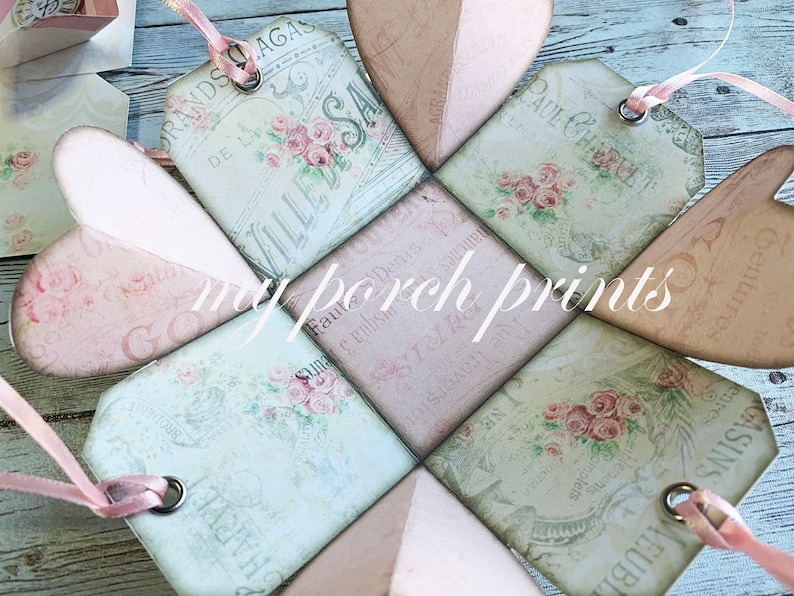 May include: A pink and green paper box with a heart shape design. The box is decorated with floral patterns and French text. The box is open and the inside is visible. The box is made of paper and has a delicate, vintage aesthetic.