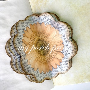 K&ouml;nnte beinhalten: Eine Papierblumen-Bastelarbeit mit einem braunen und gelben G&auml;nsebl&uuml;mchen-Design. Die Blume ist aus Seiten eines alten Buches mit deutschem Text gefertigt.