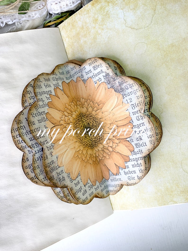 K&ouml;nnte beinhalten: Eine Papierblumen-Bastelarbeit mit einem braunen und gelben G&auml;nsebl&uuml;mchen-Design. Die Blume ist aus Seiten eines alten Buches mit deutschem Text gefertigt.