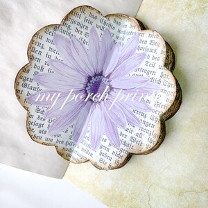 K&ouml;nnte beinhalten: Eine lila Blume mit gelbem Zentrum ist auf ein herzf&ouml;rmiges Papierhandwerk gedruckt. Das Papier ist geschichtet und hat einen Vintage-Look. Das Papier hat Text in deutscher Sprache.