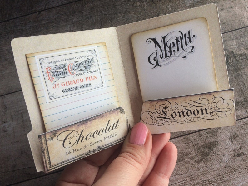 May include: A vintage-style menu card with a handwritten "Menu" title and a decorative "London" label. The card is open to reveal a small, rectangular label with the text "Chocolat 14 Rue de Sevres PARIS" and a smaller label with the text "PARFUMS AU PRINCIPE DES FLEURS Extrait Concentre POUR LE MOUCHOIR J. GIRAUD FILS GRASSE PARIS".