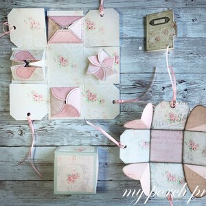 May include: Five different paper boxes with pink and white floral designs and pink ribbon accents. The boxes are folded into different shapes, including a cube, a heart, and a flower. The boxes are all decorated with a vintage style.