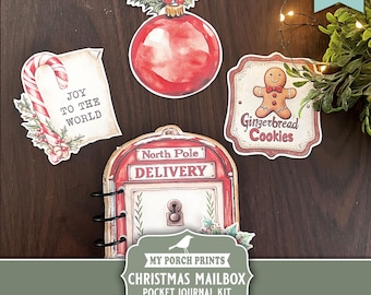 May include: A collection of Christmas-themed paper cutouts, including a red ornament, a gingerbread cookie sign, and a candy cane with the words "Joy to the World." A Christmas mailbox pocket journal kit is also featured.