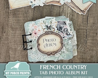 May include: A French Country tab photo album kit with a vintage aesthetic. The album features a decorative oval label that reads "Photo Album". The design includes floral and butterfly accents, with an assembled size of 4.5 x 4.75 inches.