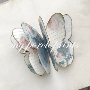 Puede incluir: Una manualidad de mariposa de papel con un patr&oacute;n de rayas azules y blancas y detalles florales. La mariposa est&aacute; doblada y tiene un efecto 3D.