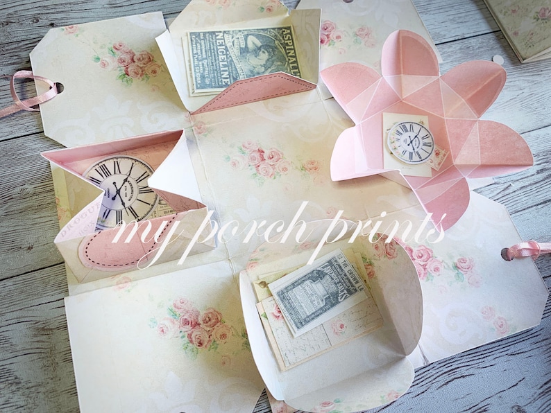 May include: A pink and white paper box with a floral design. The box is open and has several compartments. Each compartment has a different design, including a clock, a heart, and a flower. The box is perfect for storing small items or gifts.