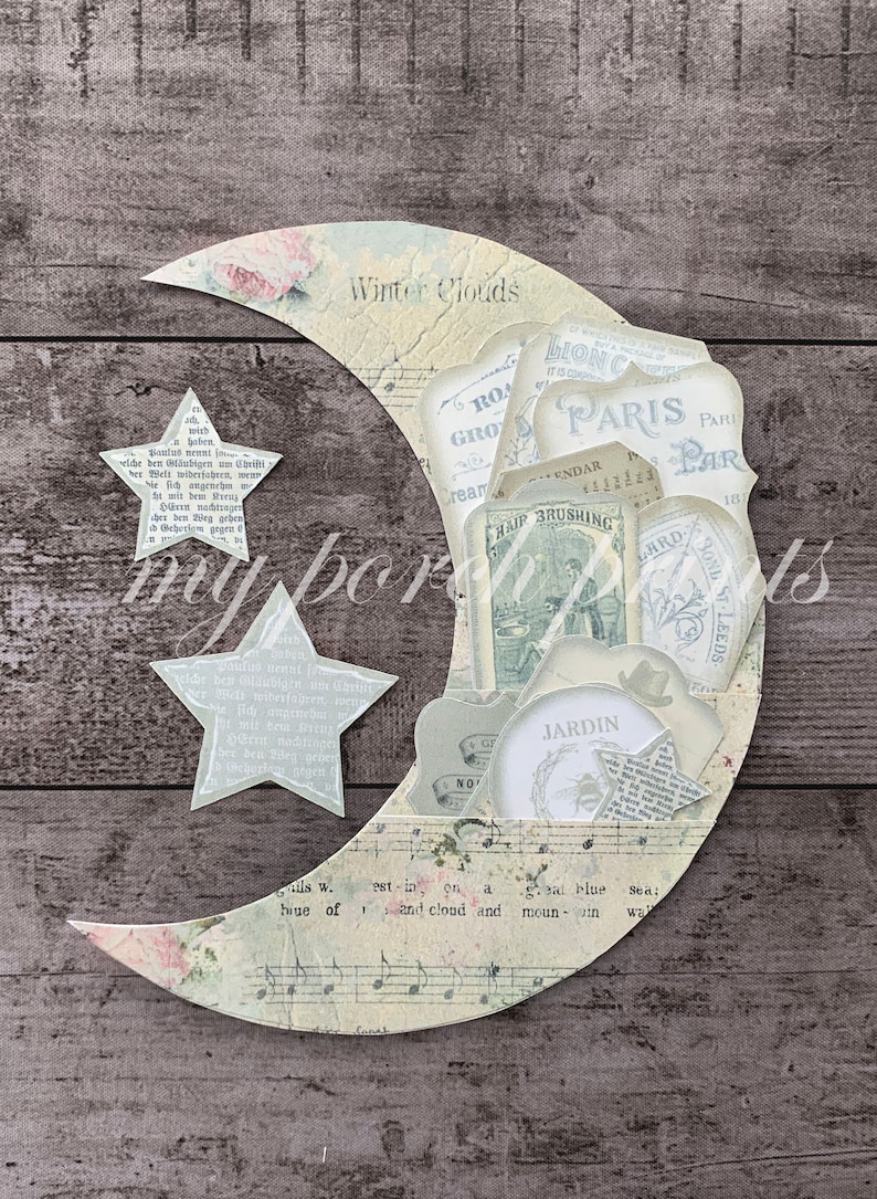 May include: A decorative moon-shaped paper craft with a vintage aesthetic. It features a crescent moon with floral and musical note patterns, filled with assorted vintage labels and two star cutouts. The text "Winter Clouds" is visible.