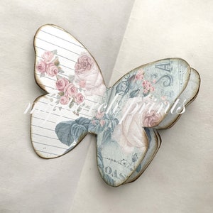 Puede incluir: Una mariposa de papel en capas con un dise&ntilde;o floral vintage. La mariposa est&aacute; hecha de m&uacute;ltiples capas de papel, cada una con un patr&oacute;n diferente. La mariposa es de color azul claro y rosa con un fondo blanco.