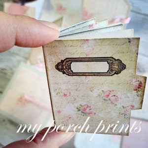 May include: A small, vintage-style journal with a floral design and a blank label. The journal is closed and has a worn, aged look.