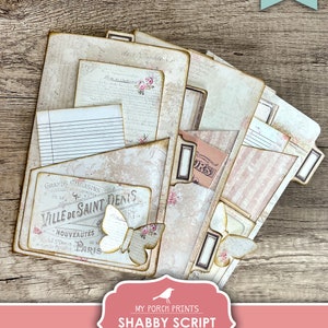 Op de afbeelding: Printbare tabbladen in shabby chic-stijl met een vintage Parijse thema. De tabbladen hebben een vlinderontwerp, schrijftekst en een bloemenpatroon. De tekst op de tabbladen luidt "Grands Magasins de la Ville de Saint Denis, Nouveaut&eacute;s de St. Denis, Paris".
