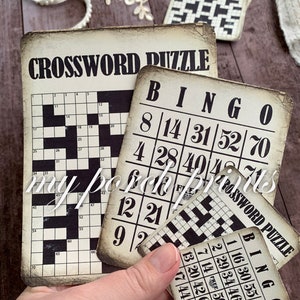 May include: Four vintage-style game cards with black and white text and numbers. The cards are for Bingo and Crossword puzzles. The cards are on a wooden surface.