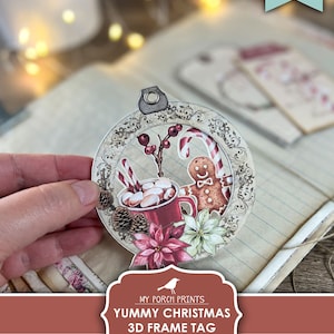 May include: Printable 3D Christmas frame tag with a red mug, marshmallows, candy canes, and a gingerbread man. The tag is decorated with a poinsettia and pine cones. "Yummy Christmas 3D Frame Tag Printable" text is on the tag.