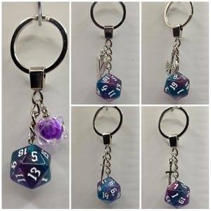 Pode incluir: Um conjunto de seis chaveiros com um chaveiro prateado com um amuleto de dado iridescente roxo e turquesa. Cada chaveiro tem um amuleto prateado diferente preso ao anel, incluindo uma espada, um machado e uma letra Y.