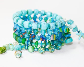 May include: A multi-strand bracelet made of blue, green, and white beads. The bracelet features a starfish charm and a variety of different bead shapes and sizes.