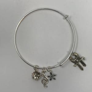 Puede incluir: Un brazalete de plata con tres abalorios: una flor, una nota musical y dos pájaros.