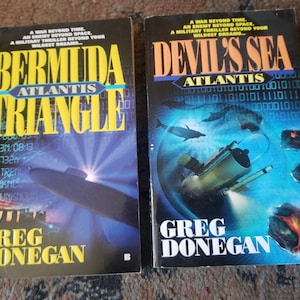 Puede incluir: Dos libros de bolsillo con portadas llamativas. "Bermuda Triangle" presenta una ilustración de submarino y texto amarillo. "Devil's Sea" tiene un fondo azul con un submarino y delfines. Ambos libros son de Greg Donegan.