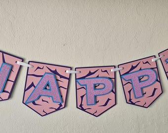 Peut inclure: Une banderole décorative composée de cinq fanions pentagonaux suspendus à un ruban blanc. Chaque fanion rose clair présente un motif craquelé violet foncé et une grande lettre violette pailletée bordée de bleu, formant le mot HAPPY.