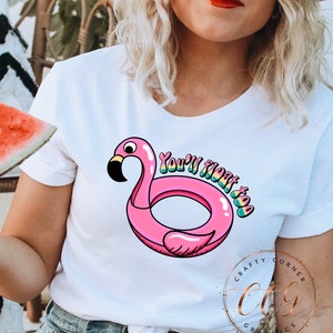 May include: White t-shirt with a pink flamingo pool float graphic and the text "You're floatin' too".