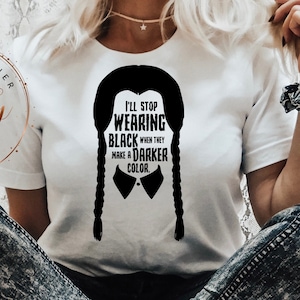 Pode incluir: Uma camiseta branca com uma silhueta preta de uma menina com tranças e o texto "Vou parar de usar preto quando eles fizerem uma cor mais escura."