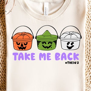May include: Cream-colored t-shirt featuring three Halloween candy buckets in orange, green, and white. The buckets have jack-o'-lantern, witch, and ghost faces. The text "TAKE ME BACK" is in purple, with "#THE90'S" below.