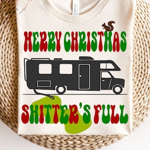 May include: A white t-shirt with a green, red and black graphic design. The graphic features a camper van with the text "Merry Christmas Shitter's Full" in a retro font.