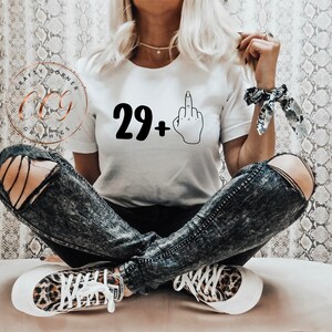 Puede incluir: Camiseta blanca con texto negro que dice "29+" y una ilustraci&oacute;n en blanco y negro de un dedo medio.