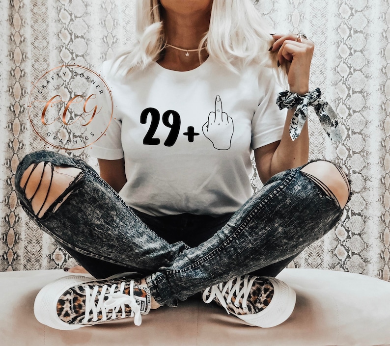 Puede incluir: Camiseta blanca con texto negro que dice "29+" y una ilustraci&oacute;n en blanco y negro de un dedo medio.