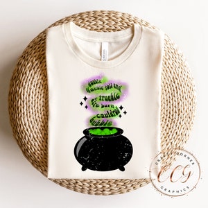 May include: A white t-shirt with a black cauldron and green potion. The text reads "Double double toil and trouble, fire burn and cauldron bubble."