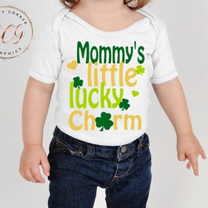 May include: White baby onesie with green shamrocks and gold lettering that reads "Mommy's little lucky charm".