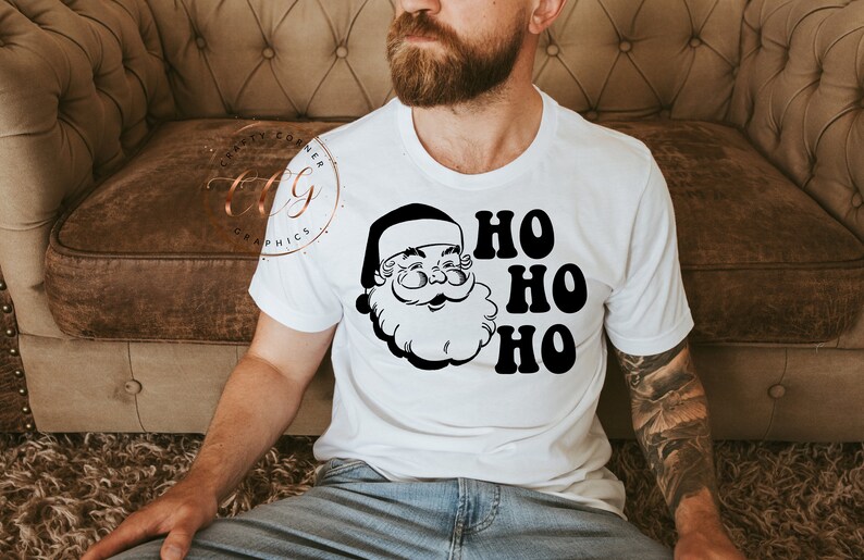 Peut inclure: T-shirt blanc avec une illustration en noir et blanc du visage du P&egrave;re No&euml;l et le texte "HO HO HO" en noir.