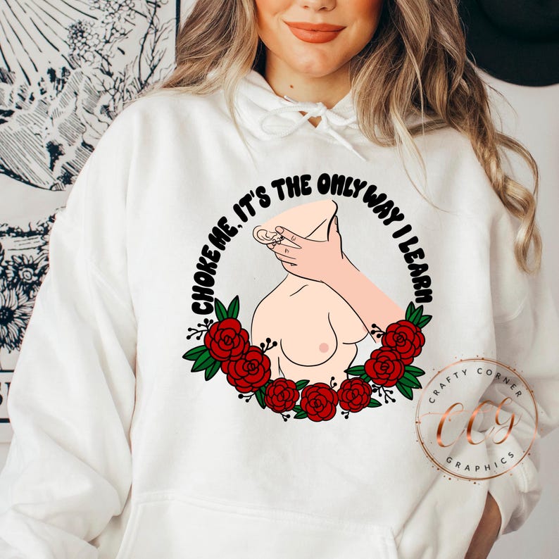 Puede incluir: Sudadera con capucha blanca con un dise&ntilde;o gr&aacute;fico. El dise&ntilde;o incluye una ilustraci&oacute;n estilizada de un torso con una mano alrededor del cuello, rodeado de rosas rojas y el texto "CHOKE ME, IT'S THE ONLY WAY I LEARN".