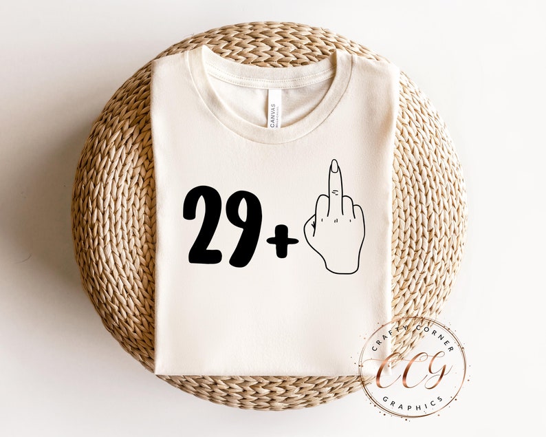 Puede incluir: Una camiseta blanca con texto negro que dice "29+" y un contorno negro de un dedo medio.