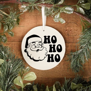 Peut inclure: Ornement de No&euml;l en c&eacute;ramique blanche avec une illustration en noir et blanc du P&egrave;re No&euml;l et le texte "HO HO HO" dans une police r&eacute;tro.
