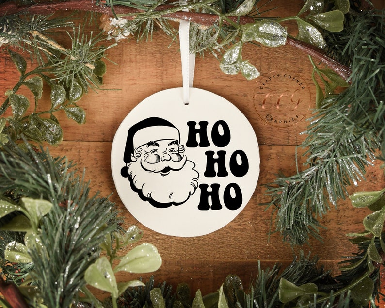 Peut inclure: Ornement de No&euml;l en c&eacute;ramique blanche avec une illustration en noir et blanc du P&egrave;re No&euml;l et le texte "HO HO HO" dans une police r&eacute;tro.