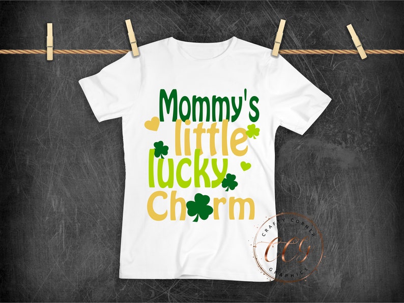 May include: White t-shirt with the text "Mommy's little lucky charm" in green, yellow, and gold lettering. The text is surrounded by shamrock designs.