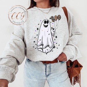 K&ouml;nnte beinhalten: Ein graues Sweatshirt mit einem wei&szlig;en Geist, der drei Ballons h&auml;lt, die "BOO" in Schwarz und Orange buchstabieren. Der Geist hat ein fr&ouml;hliches Gesicht und ist von schwarzen und orangefarbenen Konfetti umgeben.