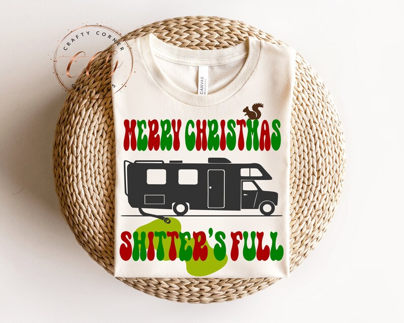 May include: A white t-shirt with a green, red and black graphic design. The graphic features a camper van with the text "Merry Christmas Shitter's Full" in a retro font.