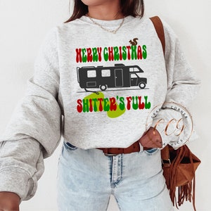 May include: A grey sweatshirt with a green, red and white graphic of a camper with the text "Merry Christmas Shitter's Full".