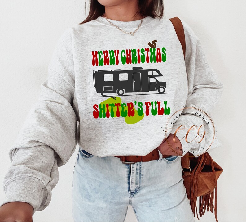 May include: A grey sweatshirt with a green, red and white graphic of a camper with the text "Merry Christmas Shitter's Full".