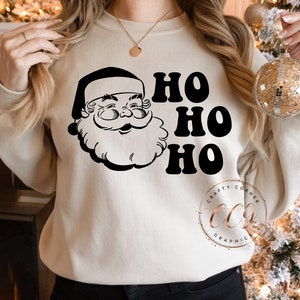 Peut inclure: Un sweat-shirt cr&egrave;me avec une illustration en noir et blanc du P&egrave;re No&euml;l et le texte "Ho Ho Ho".