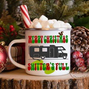 May include: White ceramic mug with a red and green "Merry Christmas" design and a black silhouette of a camper with the text "Shitter's Full" in green and red. The mug is filled with marshmallows and a red and white candy cane.