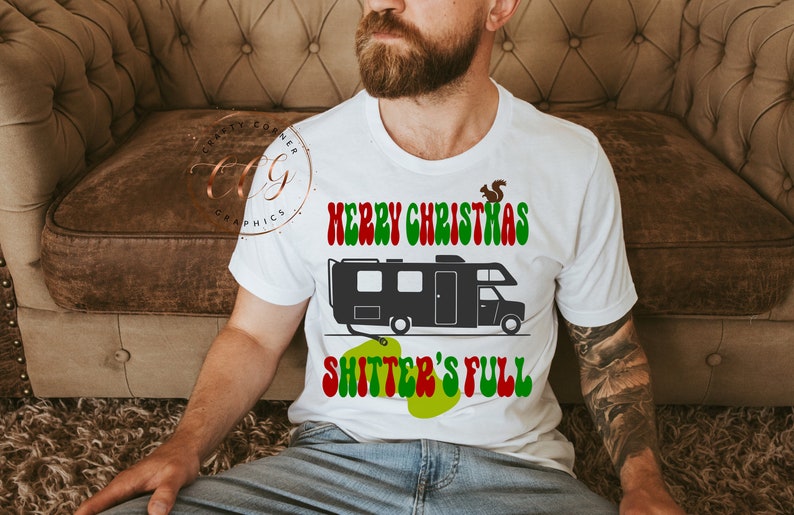 May include: White t-shirt featuring a black and white illustration of a camper van and the text "Merry Christmas Shitter's Full" in red, green, and white.