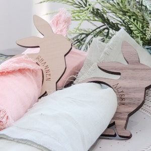 May include: Two wooden bunny napkin rings with the names "Shannon" and "Alissa" engraved on them. The rings are holding pink and light green napkins.