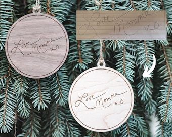 May include: Two round wooden ornaments with the handwritten message "Love Momma xo" on a blue spruce tree.