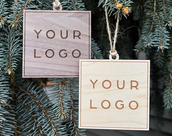 May include: Two wooden ornaments with the text "YOUR LOGO" engraved on them. The ornaments are hanging from a tree branch.