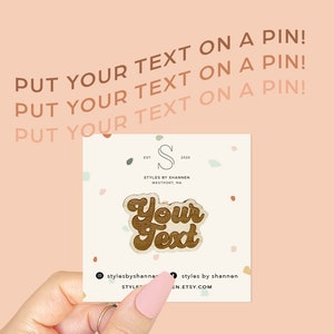 以下が含まれることがあります： レトロなフォントで「Your Text」と書かれた木製ピン。ピンは茶色で、薄い茶色の輪郭があります。ピンはピンクと白のドット柄の白いカードの上にあります。
