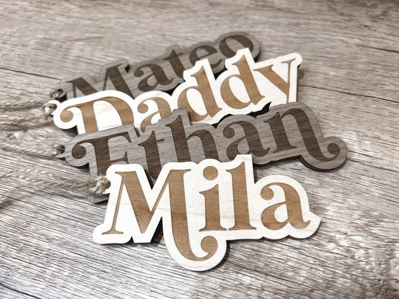 Peut inclure: Quatre &eacute;tiquettes de nom en bois avec les noms Mateo, Daddy, Ethan et Mila. Les &eacute;tiquettes sont brunes et ont un grain de bois brun clair. Les noms sont d&eacute;coup&eacute;s dans le bois et ont un contour blanc.