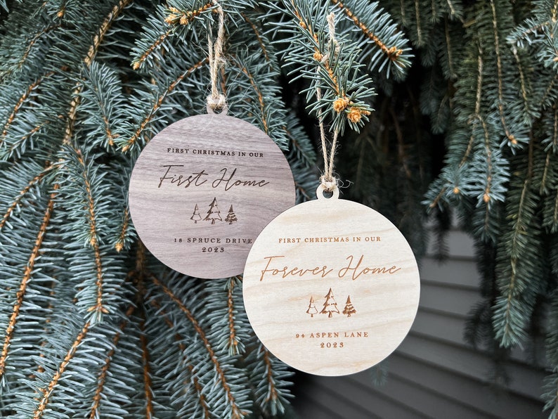 Puede incluir: Dos adornos navide&ntilde;os de madera con el texto "Primera Navidad en nuestro primer hogar" y "Primera Navidad en nuestro hogar para siempre" con el a&ntilde;o y la direcci&oacute;n.