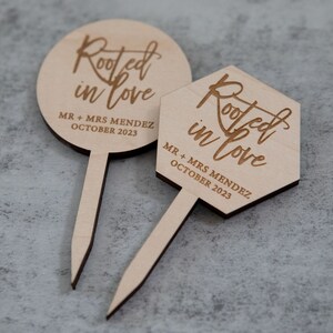 May include: Two wooden cake toppers with the text "Rooted in love" and "MR + MRS MENDEZ OCTOBER 2023".